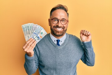 Sticker - Handsome middle age man holding dollars screaming proud, celebrating victory and success very excited with raised arm