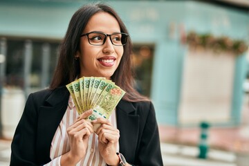 Young hispanic businesswoman holding argentina pesos banknotes at the city.