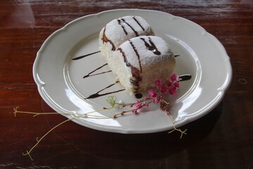 Bread of milk,  icing and chocolate decorated by pink flower on white plate.