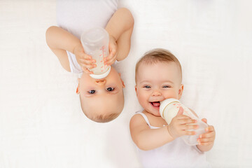 twin babies boy and girl with a bottle of milk on a white bed at home, baby food concept, place for 