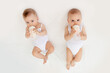 © Any Grant - two baby twins boy and girl with a bottle of milk on a white bed at home, baby food concept, place for text
