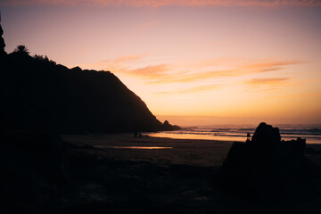 Dark evening view of ocean and high rocks on sandy shore with sunset on horizon, breathtaking scenery of marine and yellow sundown