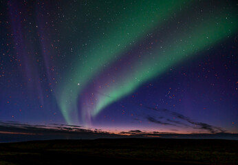 double band northern lights in iceland. rocky foreground with the last glimmer of sun on the horizon