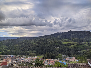 Wall Mural - Aerial view of colorful buildings surrounded by mountain forests under the cloudy sky