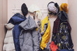 Many winter coats and caps, hats hanging in a mess on hooks in a corridor, decluttering warm clothes