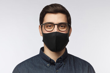 Poster - Young man wearing denim shirt, glasses and black mask standing isolated on gray background