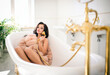 Sensual brunette woman in fur coat lying in the tub. Sexy young woman with curly hair and straight beautiful body takes a shower