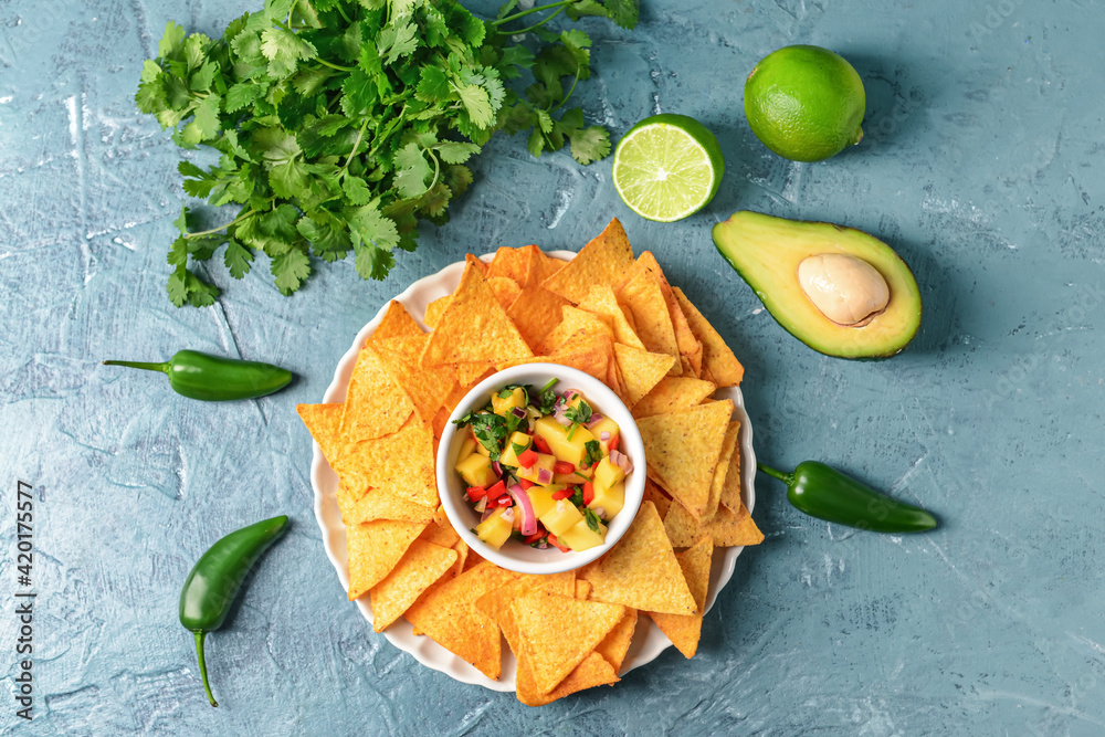 Plate with fresh mango salsa and nachos on color background