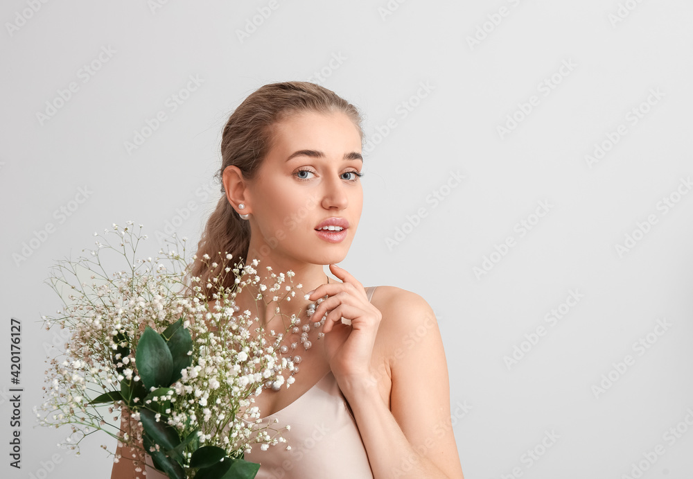 Beautiful young woman with flowers on light background