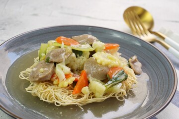 Wall Mural - A plate of I Fu Mie or Crispy Fried Noodle with thick savory sauce and meatball and vegetables in shiny and grainy white background. Selective focus