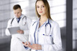 © cameravit - Professional woman doctor with a stethoscope is using a computer tablet, while she is standing together with her colleague in a clinic. Young doctors at work in a hospital. Medicine and healthcare