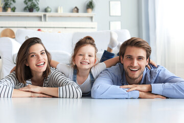 Young Caucasian family with small daughter pose relax on floor in living room, smiling little girl kid hug embrace parents, show love and gratitude, rest at home together.