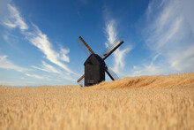 An Old Wooden Windmill Stands In A Wheat Field With A Beautiful Blue Sky