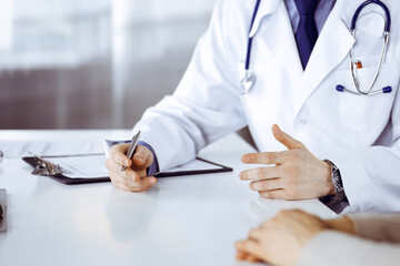 Unknown male doctor and patient woman discussing something while sitting in clinic and using clipboard. Best medical service in hospital, medicine, pandemic stop