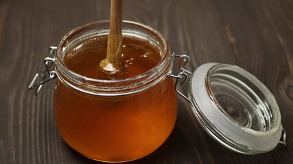 Wall Mural - A jar of honey with a honey dipper spoon. A trickle of honey dripping into the jar