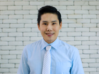 Portrait of young and handsome Asian man wearing shirt and tie with smile and happy friendly face on white brick wall background.