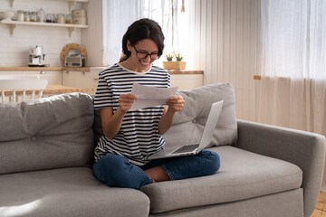 Overjoyed millennial woman sitting on couch at home, holding and reading paper document, feel euphoric. American girl gets a job, enjoys exam results or university acceptance letter. Good news.