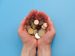 Hands full of coins on blue background. Closeup. Saving money concept