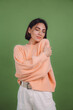 © Анастасия Каргаполов - Young woman in casual peach sweater isolated on green olive color background love concept, holding hands crossed hugging herself