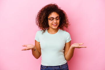 Wall Mural - Young african american woman isolated on pink background holding something with palms, offering to camera.