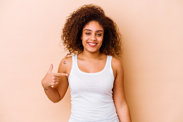 Wall Mural - Young african american woman isolated on beige background person pointing by hand to a shirt copy space, proud and confident