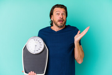 Wall Mural - Middle age dutch man holding a scale isolated on blue background surprised and shocked.