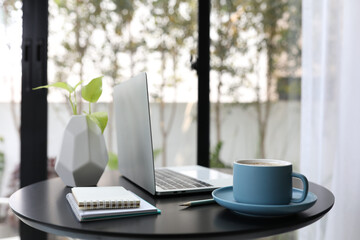 Blue coffee cup with laptop and notebooks on black wooden table