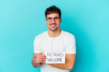 Wall Mural - Young caucasian man holding a Refugees welcome placard isolated laughing and having fun.