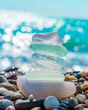Sea Glass Stones Arranged In A Balance Pyramid On The Beach. Beautiful Azure Color Sea With Blurred Seascape Background. Meditation And Harmony Concept.