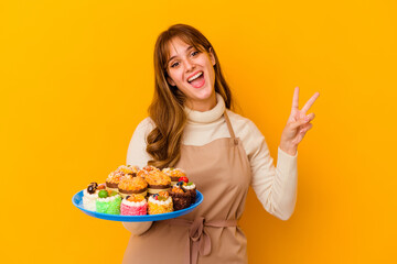 Wall Mural - Young pastry chef woman isolated on yellow background joyful and carefree showing a peace symbol with fingers.