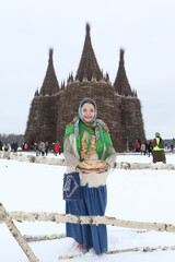 Wall Mural - Maslenitsa 2021. Traditional national holiday: Maslenitsa. Russian woman in folk clothes, Pavlovo Posad shawl, scarf. Maslenitsa in Nikola-Lenivets, Kaluga region, Russia. Wooden castle. Pancakes