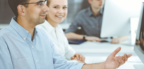 Business people working together in modern office. Happy smiling adult businessman using pc computer with colleagues. Teamwork and partnership concept