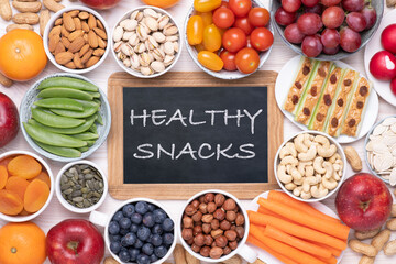 Healthy snacks such as fresh fruits, vegetables and nuts on white wooden table, top view