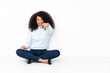 © luismolinero - Young african american woman sitting on the floor surprised and pointing front