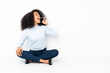© luismolinero - Young african american woman sitting on the floor keeping a conversation with the mobile phone
