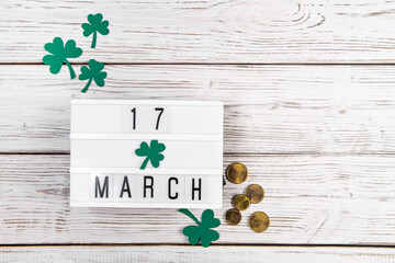 Flatlay for St. Patricks Day. Gold coins and shamrock clover leaves on a white wooden background. Happy Irish holiday, symbols of luck.