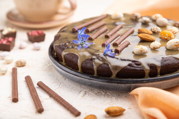 Homemade chocolate brownie cake with caramel cream and almonds with cup of coffee on a white concrete  background. Side view, selective focus.