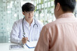 © Puwasit Inyavileart - Young Asian man in a white robe talks to a man, Doctors diagnose diseases and give advice or treatment solutions to patients in the hospital examination room, Explaining medical examination results.