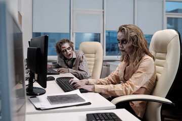 Poster - Young spooky zombie businesswoman sitting by desk in front of computer monitor and networking