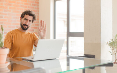 Sticker - young bearded man looking serious, stern, displeased and angry showing open palm making stop gesture and working with a laptop