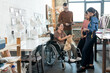 © pressmaster - Group of young fashion designers surrounding disable seamtsress in wheelchair during discussion