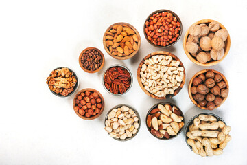 Wall Mural - Assortment of nuts in bowls. Cashews, hazelnuts, walnuts, pistachios, pecans, pine nuts, peanuts, macadamia, almonds, brazil nuts. Food mix on white background, top view, copy space