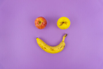 Top view of two apples and a banana drawing a smile on a lilac background