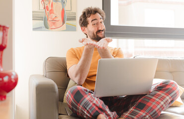 young bearded man smiling happily with friendly, confident, positive look, offering and showing an object or concept and sitting with a laptop