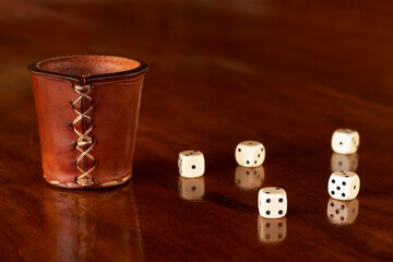 Closeup in six dices and a leather cup in wooden table with reflection. Brazilian game aka Bozó.