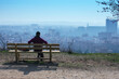 Woman from behind sitting on bench with city in background