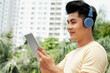 © DragonImages - Asian young man in headphones watching something online on digital tablet in the city
