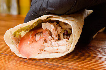 Wall Mural - Burrito making process. The chef wraps stuffed pita on a wooden table. Mexican dish.