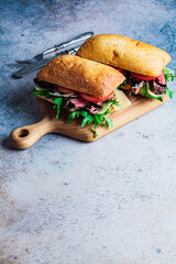 Canvas Print - Beef sandwich with arugula, tomato and parmesan on wooden board, copy space. Comfort food concept.