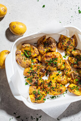 Canvas Print - Baked smashed potatoes with herbs in white oven dish, top view.